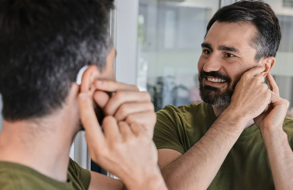 Adult Checking Discreet Hearing Aid Fit In A Bathroom Mirror